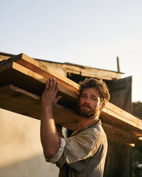 Young man carrying rough sawn timber boards across a yard