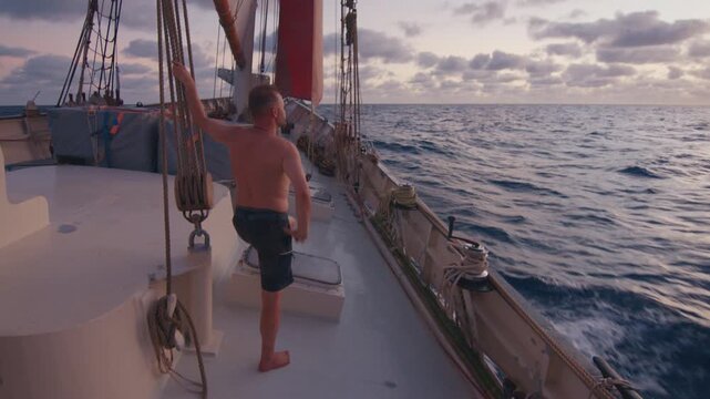 Sailing the Atlantic. Male sailor stands on the deck of the big sailing boat moving in the Atlantic Ocean under the sails and enjoys the first light of the day
