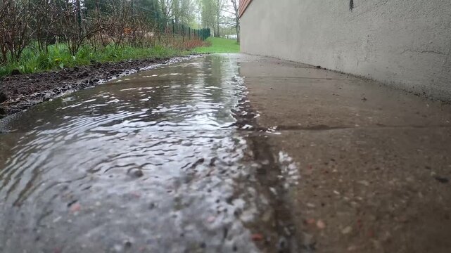 Rainwater flowing along concrete path beside house