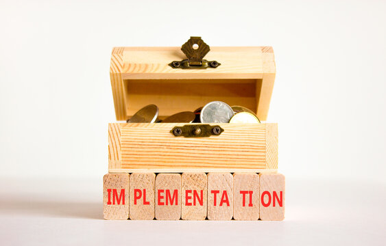 Implementation word symbol. Concept word Implementation on beautiful wooden blocks. Beautiful white table white background. Wooden chest with coins. Business implementation word concept. Copy space.