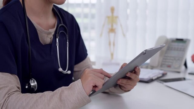 Asian female doctor reviewing digital patient records on tablet in modern medical clinic office