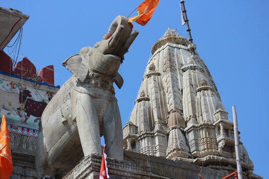 Stone elephant guard statue with a flag in front of the carved shikhara tower of the historic Jagdish Temple in Udaipur.