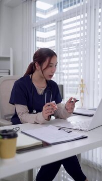 Young Asian female doctor explaining anatomical model during telemedicine consultation at modern clinic desk