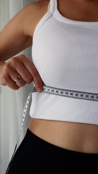 Woman measuring underbust circumference with tape measure for bra sizing.
