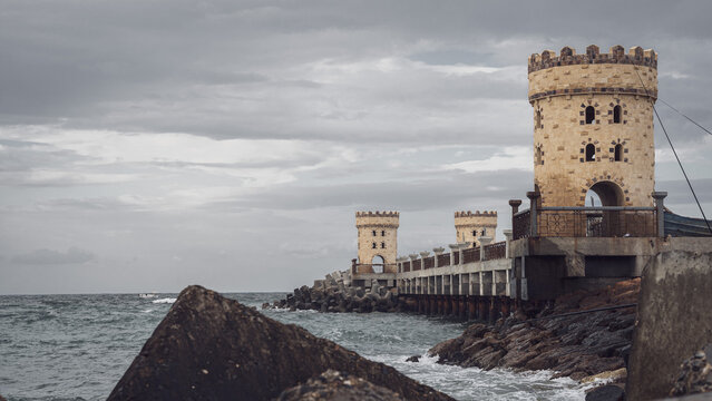View of the historic Montaza Palace towers and bridge extending into the Mediterranean Sea under a cloudy sky in Alexandria, Alexandria Governorate, Egypt.