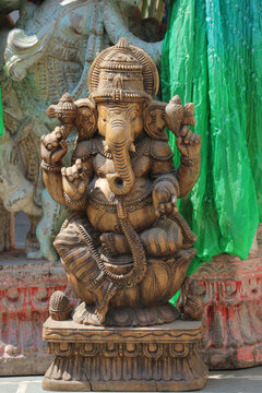 Full length vertical view of a traditional carved wooden Hindu god Lord Ganesha statue sitting on a lotus pedestal.