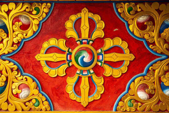 View of a colorful Buddhist Vajra symbol carved in relief on a temple wall, featuring intricate gold, red, and blue patterns in Pokhara, Gandaki Province, Nepal.