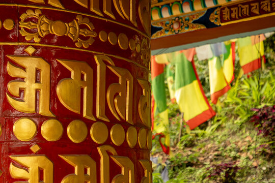 View of a traditional red and gold Buddhist prayer wheel with intricate inscriptions, set against a backdrop of colorful prayer flags in Pokhara, Gandaki Province, Nepal.