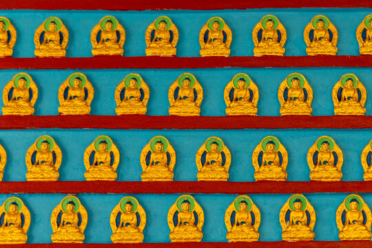 View of rows of small golden Buddha statues arranged on a blue wall with red horizontal stripes in Pokhara, Gandaki Province, Nepal.