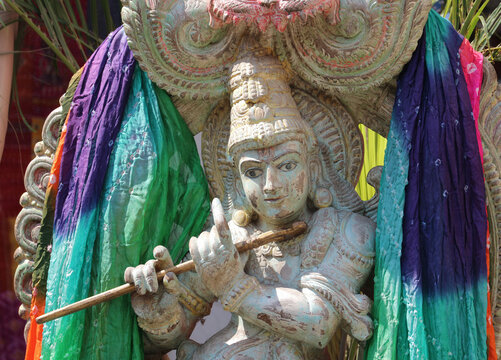 Close-up of a traditional Hindu god Lord Krishna statue playing the flute decorated with vibrant colorful silk fabrics.