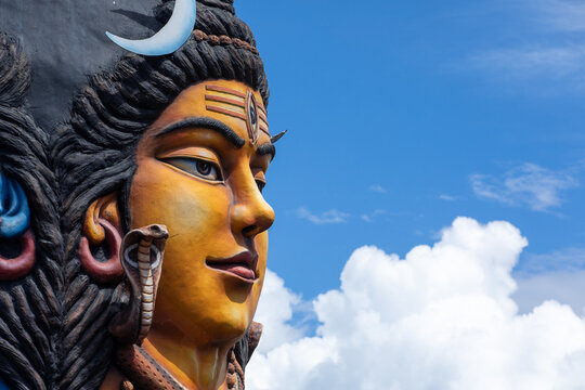 View of the colorful Lord Shiva statue against a bright blue sky with white clouds in Pokhara, Gandaki Province, Nepal.