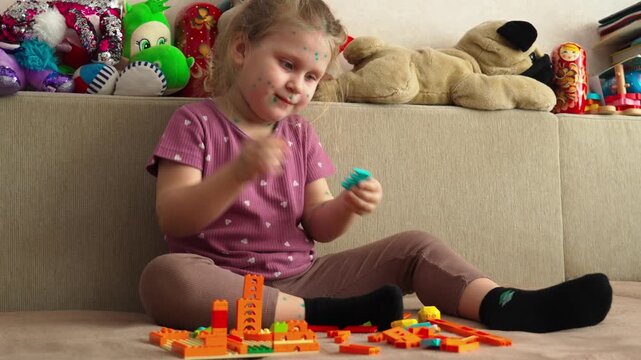 A little girl with chickenpox is playing at home with a construction kit. The child is in home isolation. Chicken pox.