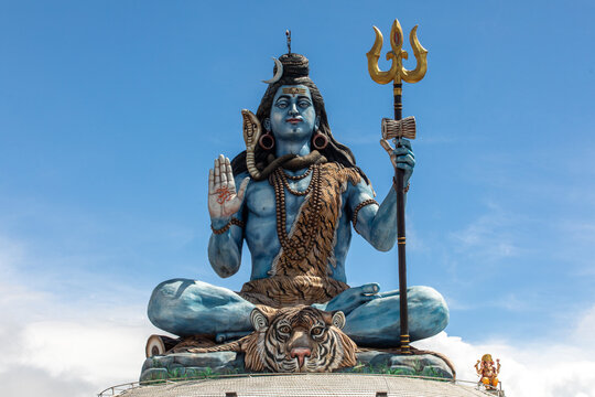 View of the large blue statue of Lord Shiva sitting in a meditative pose with a trident and a tiger skin, set against a clear blue sky in Pokhara, Gandaki Province, Nepal.