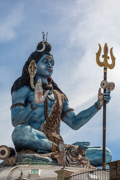 View of the large blue statue of Lord Shiva holding a trident and sitting on a tiger skin against a bright sky in Pokhara, Gandaki Province, Nepal.