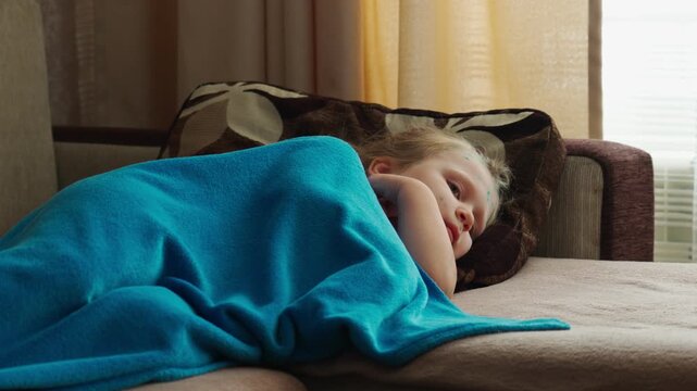 A little girl with chickenpox lies sadly at home, covered with a blanket.  The child is in home isolation. Chicken pox.