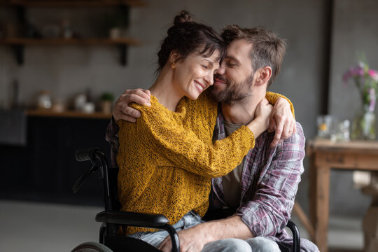 Loving couple embracing at home, one partner in a wheelchair, showing affection