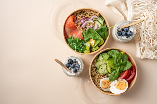 Healthy protein bowls with smoked salmon, egg, quinoa, avocado, spinach, cucumber and chuka seaweed salad in cardboard containers, served with chia seed yogurt and blueberries 