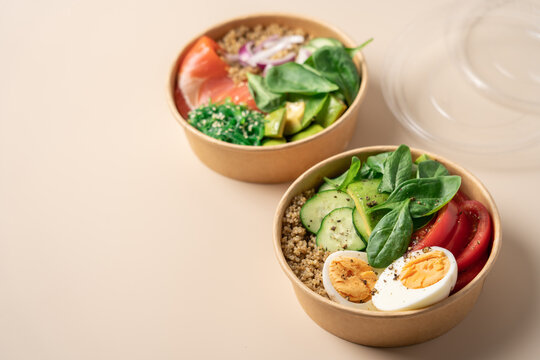 Healthy protein bowls with smoked salmon, egg, quinoa, avocado, spinach, cucumber and chuka seaweed salad in cardboard containers on a light beige background, nutritious balanced meal concept