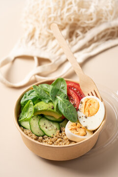 Healthy protein bowl with egg, avocado, spinach, cucumber and quinoa in a cardboard container on a light beige background, nutritious balanced meal concept 
