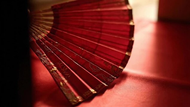Elegant red folding fan with intricate details displayed on a textured surface