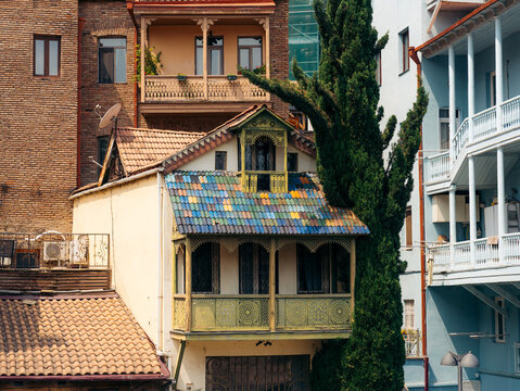 View of Old Tbilisi featuring a historic house with a colorful tiled roof, intricate wooden balconies, and a tall cypress tree in Tbilisi, Tbilisi, Georgia.