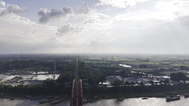Aerial drone footage of Hardinge Bridge crossing the Padma River, with green riverbanks, rural settlements, agricultural fields, waterways and scattered clouds visible across Bangladesh.