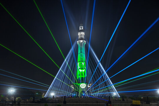 View of the Minar-e-Pakistan monument illuminated with vibrant green and blue laser light beams against the night sky in Lahore, Punjab, Pakistan.