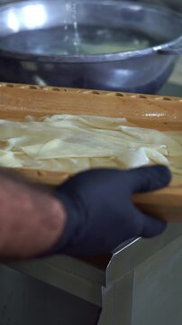 Chef in black gloves holding a wooden platter filled with freshly boiled dough sheets for beshbarmak