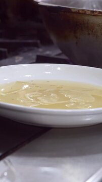 Chef straining boiled dough sheets for beshbarmak using a wire skimmer into a white plate