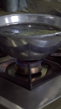 Chef putting fresh dough sheet into boiling water in a cauldron over gas stove burner