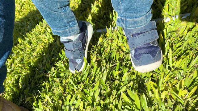Close up of a little child's feet wearing blue sneakers dangling over fresh green grass in a garden