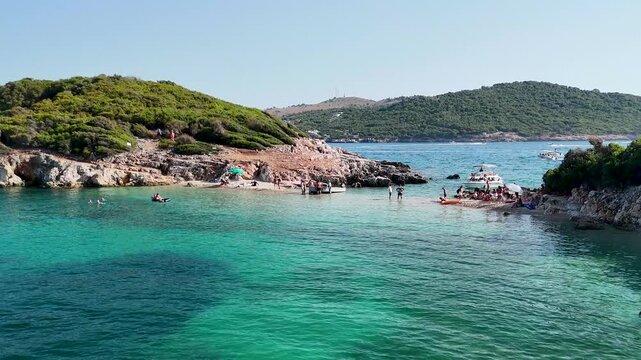 Aerial view of people relaxing on Twin Islands beach of Ksamil, crystal clear sea, Ionian Sea, Saranda, Albania. Drone view from above. Sandy beach and people relaxing in sea. Summer destination on th