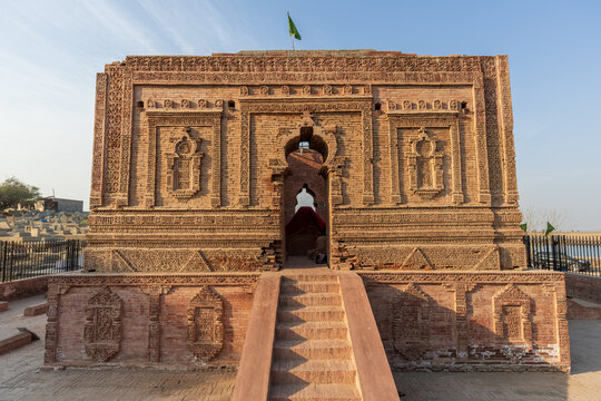 View of the historic Tomb of Saidan Shaheed with intricate brickwork carvings, arched entrance, and surrounding cemetery grounds in Multan, Punjab, Pakistan.