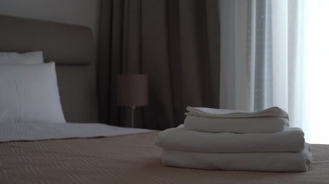 Stack of white cotton towels placed on a hotel bed by female hands, clean hospitality and comfortable accommodation concept