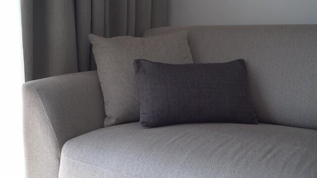 Woman&rsquo;s hands placing a cushion on a gray sofa in a cozy living room, home comfort and interior styling concept