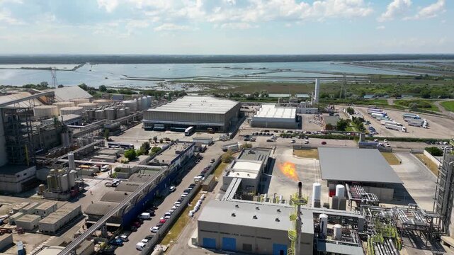 Aerial drone view of red gas tanker ship docked at Ravenna port near chemical refinery plant with gas flare stack burning bright on sunny day in Emilia Romagna Italy 