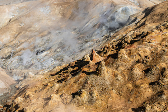 View of the geothermal landscape at Kerlingarfjoll with rising steam vents, rugged volcanic rock formations, and vibrant orange-hued terrain, Hrunamannahreppur, Iceland.