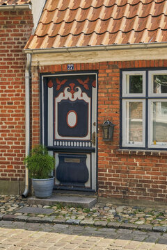 View of a historic brick house with a decorative blue door, cobblestone street, and potted plant in Ribe, Denmark.