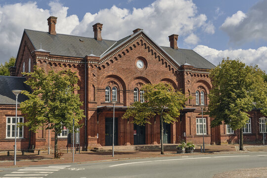 View of the historic red brick Ribe Railway Station with arched windows and a clock on the facade, surrounded by trees in Ribe, Denmark.