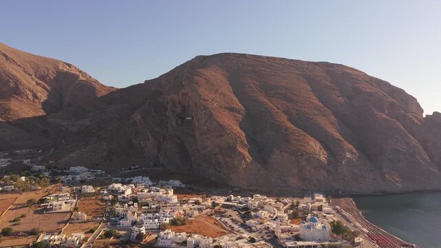 Drone view of Perissa village nestled against massive Mesa Vouno mountain rock face in Santorini Greece