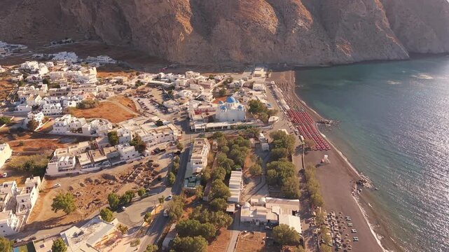 Drone shot over Perissa black sand beach resort area and Perissa Beach Kiosk church Santorini Greece