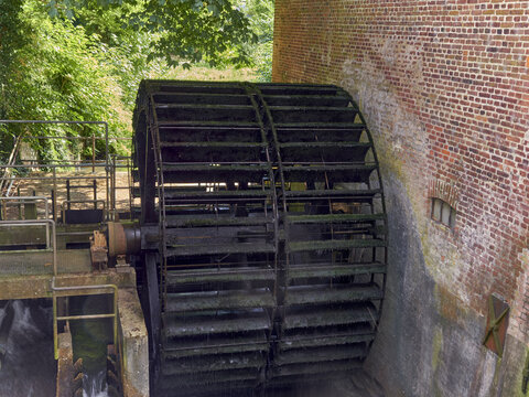 View of a large, moss-covered watermill wheel spinning beside a rustic brick building in Ribe, Denmark.