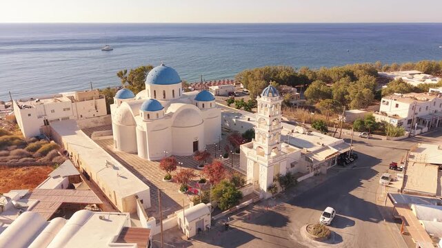 Drone shot circling Perissa Beach Kiosk blue domed church with bell tower in Santorini Greece