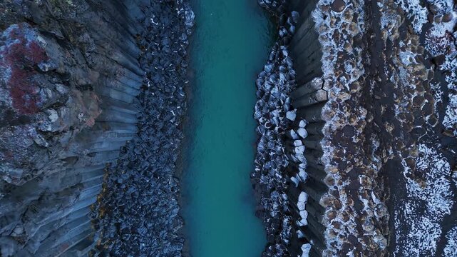 Top down aerial shot of turquoise glacial river flowing between basalt rock cliffs in Stu&eth;lagil Iceland