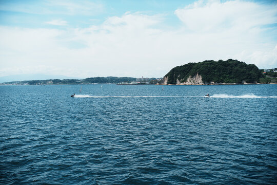 View of jet skis speeding across the blue water near the coastal cliffs of Hayama, Kanagawa, Japan.