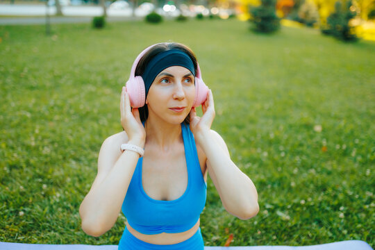Portrait of a fit girl adjusting pink headphones before training in the park.