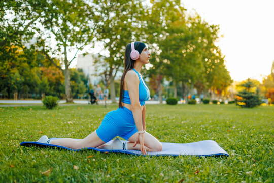 Side view of an athletic woman practicing a yoga stretch in the summer park.