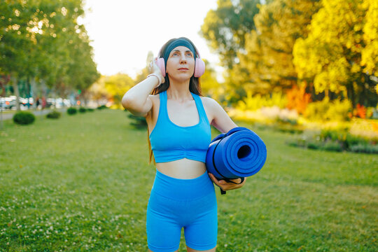 Athletic young woman carrying a yoga mat in the green park.