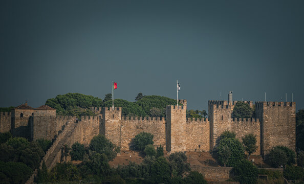 View of Castelo de Sao Jorge with its historic stone walls and battlements surrounded by lush trees under a clear sky in Lisboa, Lisboa, Portugal.