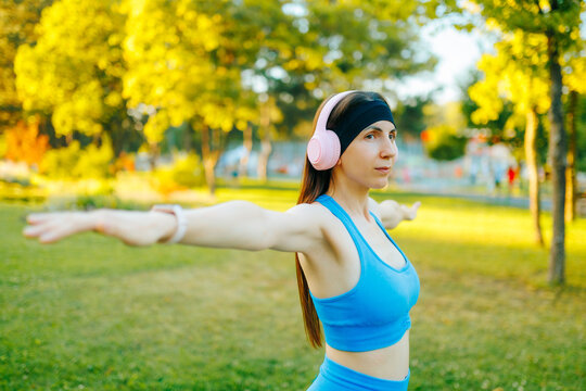Active fit woman practicing arm stretching exercises in the sunny park.